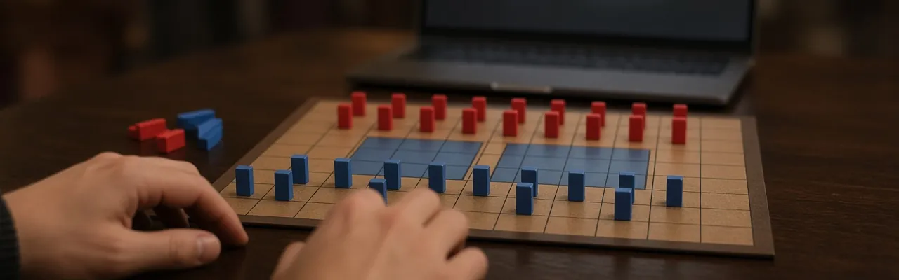 A Stratego board mid-game on a wooden table, red and blue pieces standing in formation, with a player's hands on one side and an open laptop across from them.